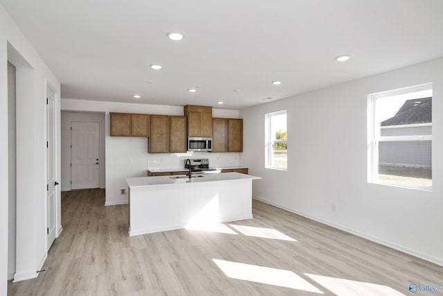 kitchen with sink, light wood-type flooring, an island with sink, and appliances with stainless steel finishes