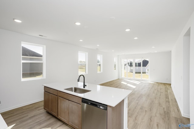 kitchen featuring a center island with sink, sink, stainless steel dishwasher, and light hardwood / wood-style flooring