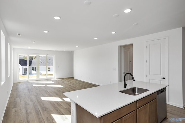 kitchen featuring sink, stainless steel dishwasher, an island with sink, and light wood-type flooring