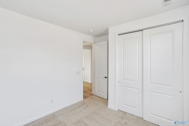 unfurnished bedroom with light colored carpet and a closet