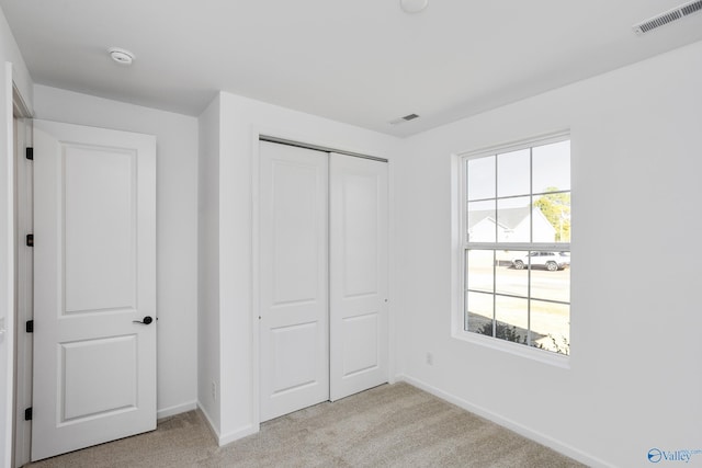 unfurnished bedroom featuring multiple windows, light colored carpet, and a closet