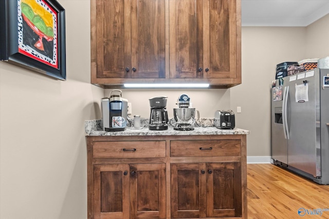 kitchen with stainless steel fridge with ice dispenser, light stone countertops, and light hardwood / wood-style flooring