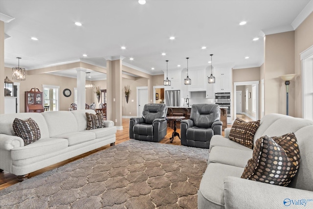 living room featuring decorative columns, sink, wood-type flooring, and ornamental molding