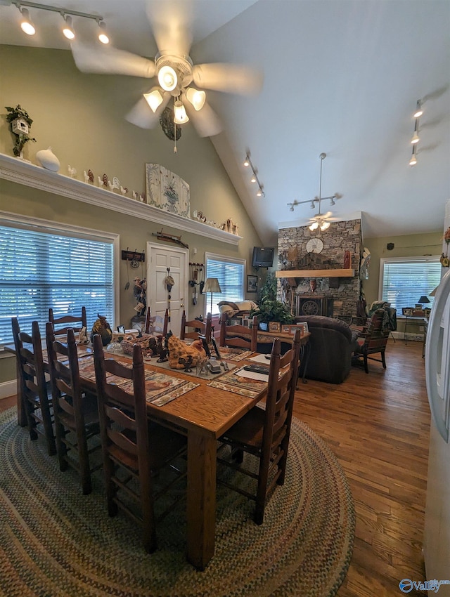 dining space featuring track lighting, a stone fireplace, high vaulted ceiling, ceiling fan, and wood-type flooring