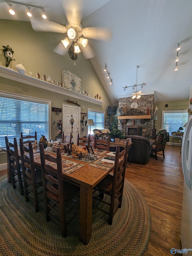 dining room featuring a fireplace, ceiling fan, track lighting, wood finished floors, and high vaulted ceiling