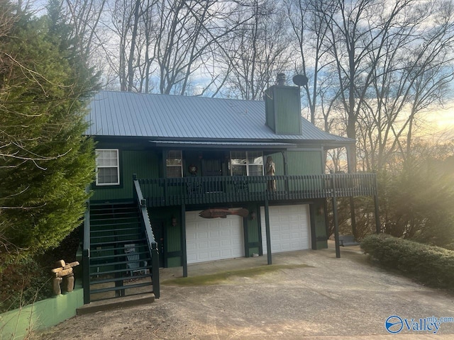 view of front of home with a chimney, an attached garage, metal roof, driveway, and stairs