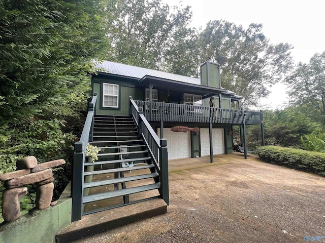 back of property featuring metal roof, a garage, driveway, stairway, and a chimney