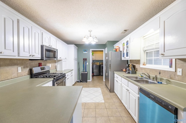 kitchen featuring stainless steel appliances, a sink, white cabinets, hanging light fixtures, and glass insert cabinets