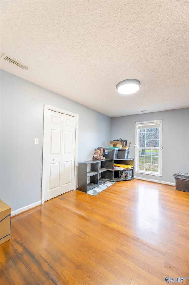 unfurnished office featuring visible vents, a textured ceiling, baseboards, and wood finished floors