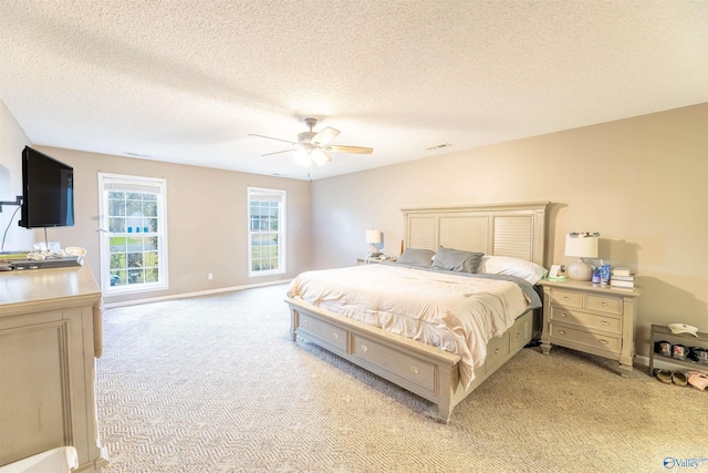 bedroom with baseboards, visible vents, a ceiling fan, light colored carpet, and a textured ceiling