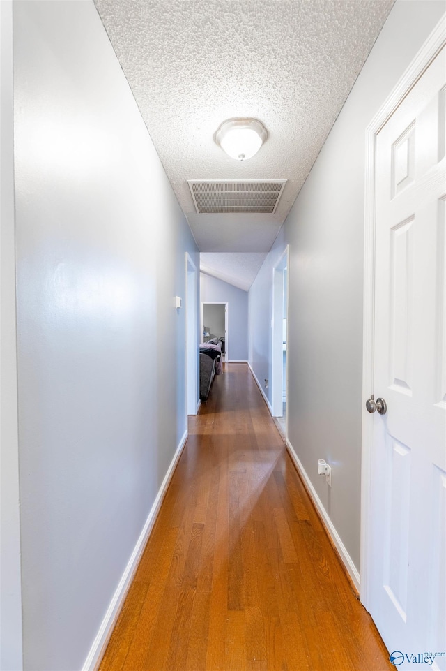 hall with lofted ceiling, visible vents, a textured ceiling, wood finished floors, and baseboards