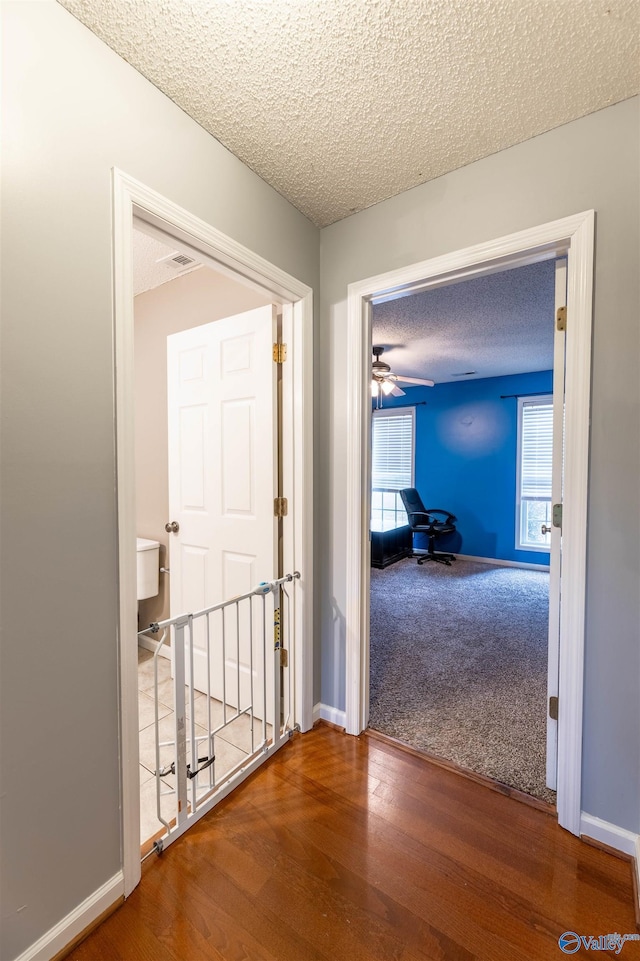 hallway featuring a textured ceiling, wood finished floors, and baseboards