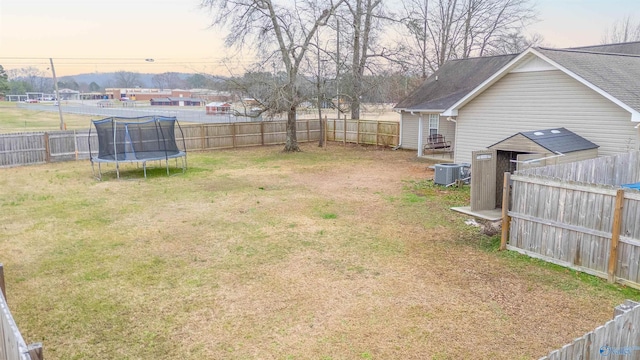 view of yard featuring a trampoline, a fenced backyard, and central air condition unit