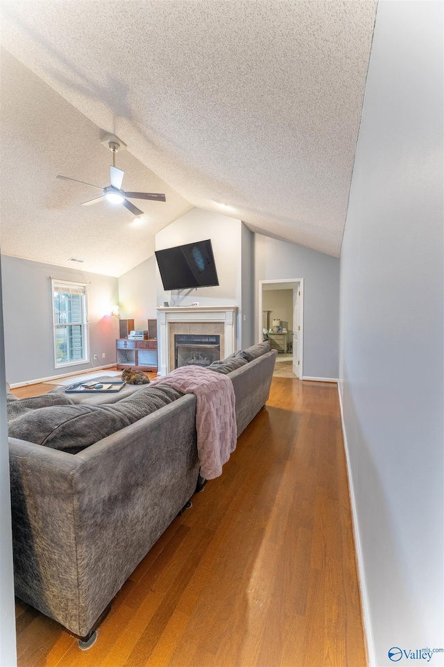 living area with a textured ceiling, a tile fireplace, wood finished floors, baseboards, and vaulted ceiling