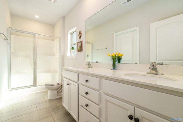 bathroom featuring double vanity, toilet, a stall shower, and a sink