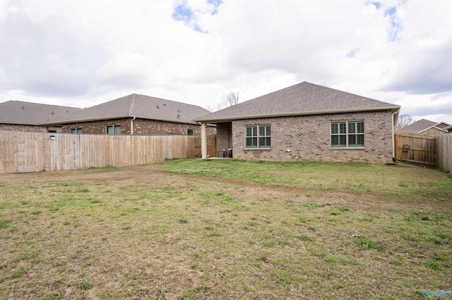 rear view of house featuring brick siding, a fenced backyard, and a yard