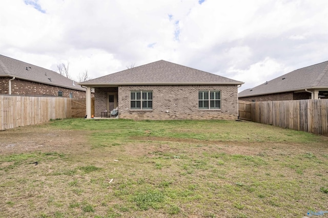 rear view of property featuring brick siding, a lawn, and a fenced backyard