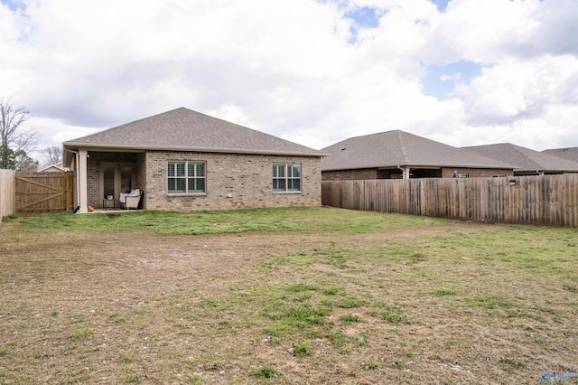 back of property featuring a lawn, brick siding, a fenced backyard, and roof with shingles