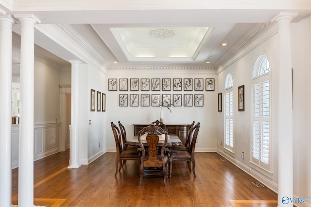 dining area featuring wood-type flooring, a raised ceiling, decorative columns, and ornamental molding