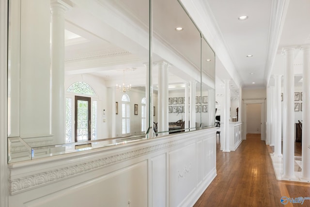 hall with wood-type flooring, a notable chandelier, decorative columns, and ornamental molding