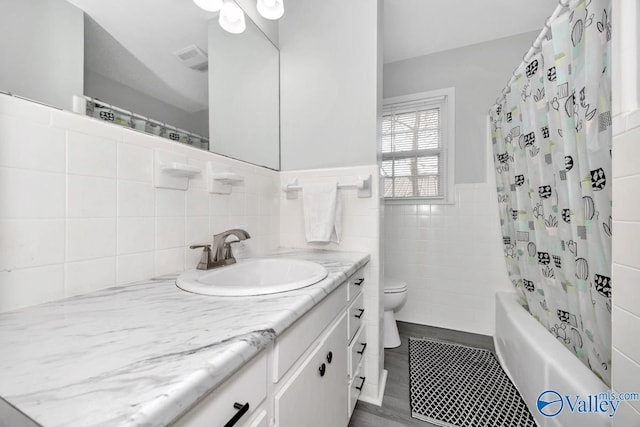 bathroom with tile walls, shower / bath combination with curtain, visible vents, toilet, and vanity