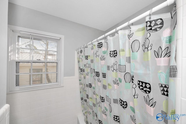 bathroom featuring a wainscoted wall, shower / bath combination with curtain, and tile walls