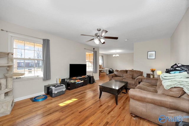 living room with light wood-style floors, baseboards, and ceiling fan with notable chandelier