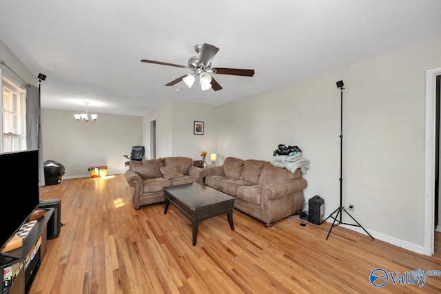 living area featuring ceiling fan with notable chandelier, light wood-style flooring, and baseboards