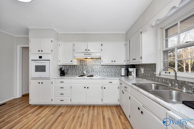 kitchen featuring white cabinets, a sink, light wood-type flooring, white appliances, and under cabinet range hood