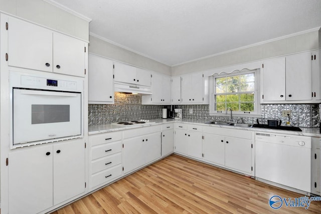 kitchen featuring under cabinet range hood, white appliances, a sink, light wood-type flooring, and crown molding