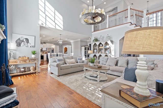 living room featuring wood-type flooring, an inviting chandelier, a high ceiling, and ornamental molding