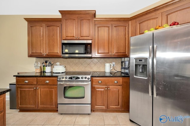 kitchen with backsplash, light tile patterned floors, stainless steel appliances, and dark stone counters