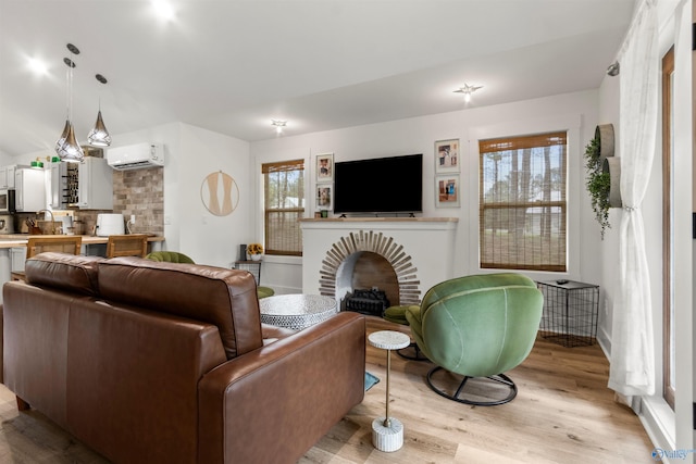 living room with a wall mounted air conditioner, light hardwood / wood-style flooring, and a brick fireplace