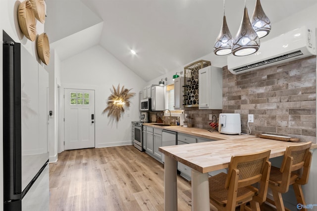 kitchen with gray cabinetry, hanging light fixtures, butcher block countertops, an AC wall unit, and appliances with stainless steel finishes