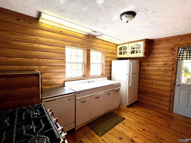 kitchen featuring white appliances, light wood-style flooring, a textured ceiling, rustic walls, and a sink