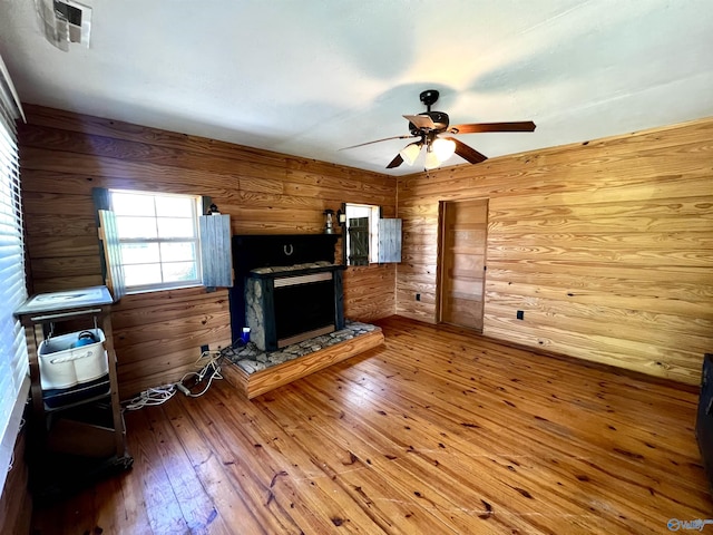 unfurnished living room featuring wooden walls, visible vents, a ceiling fan, and hardwood / wood-style floors