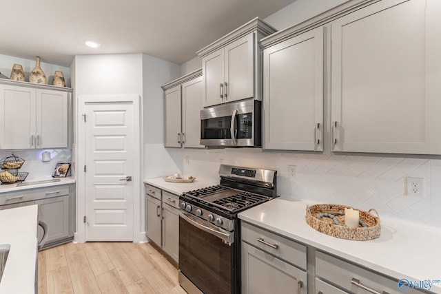 kitchen with stainless steel appliances, gray cabinetry, decorative backsplash, and light wood-style floors