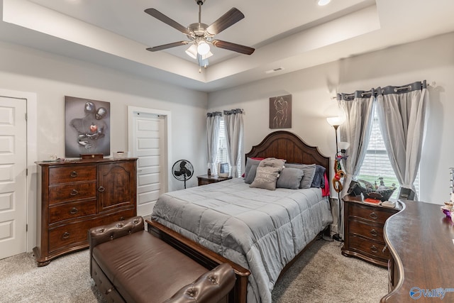 bedroom featuring a raised ceiling, light carpet, and a ceiling fan