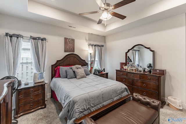 bedroom with light colored carpet, ceiling fan, visible vents, and a raised ceiling