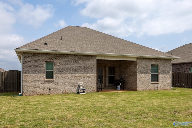 back of property with fence, a patio, roof with shingles, brick siding, and a lawn