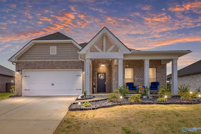 view of front of house with a porch, brick siding, a yard, an attached garage, and concrete driveway