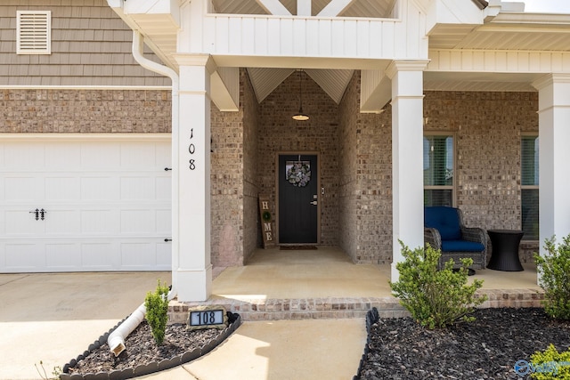 view of exterior entry featuring visible vents, covered porch, an attached garage, and brick siding