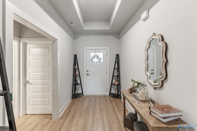 foyer entrance with a tray ceiling, visible vents, baseboards, and light wood-type flooring