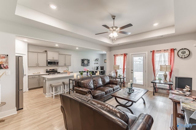 living room with a ceiling fan, a tray ceiling, recessed lighting, and light wood-style flooring