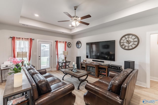 living area featuring light wood-type flooring, a raised ceiling, ceiling fan, and a healthy amount of sunlight