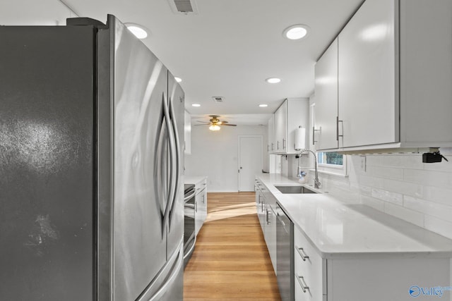 kitchen with sink, appliances with stainless steel finishes, tasteful backsplash, white cabinets, and light wood-type flooring