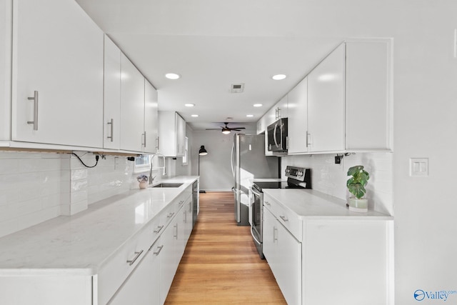 kitchen featuring light wood-type flooring, appliances with stainless steel finishes, white cabinets, ceiling fan, and backsplash