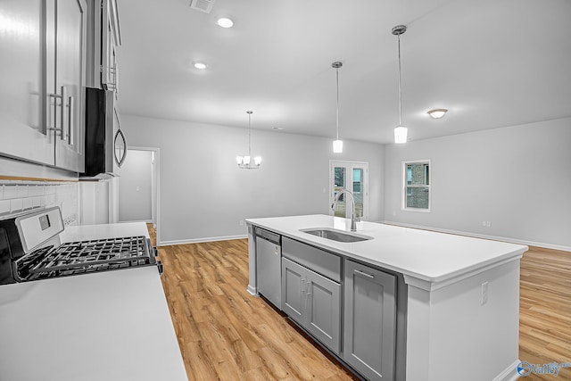 kitchen with sink, appliances with stainless steel finishes, gray cabinets, pendant lighting, and a kitchen island with sink