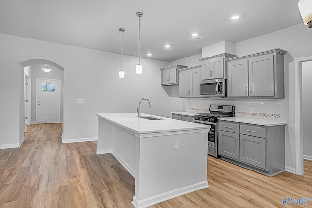 kitchen featuring sink, light wood-type flooring, an island with sink, pendant lighting, and stainless steel appliances