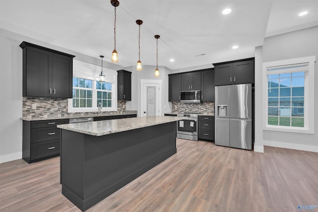 kitchen featuring a kitchen island, pendant lighting, light hardwood / wood-style floors, stainless steel appliances, and light stone countertops